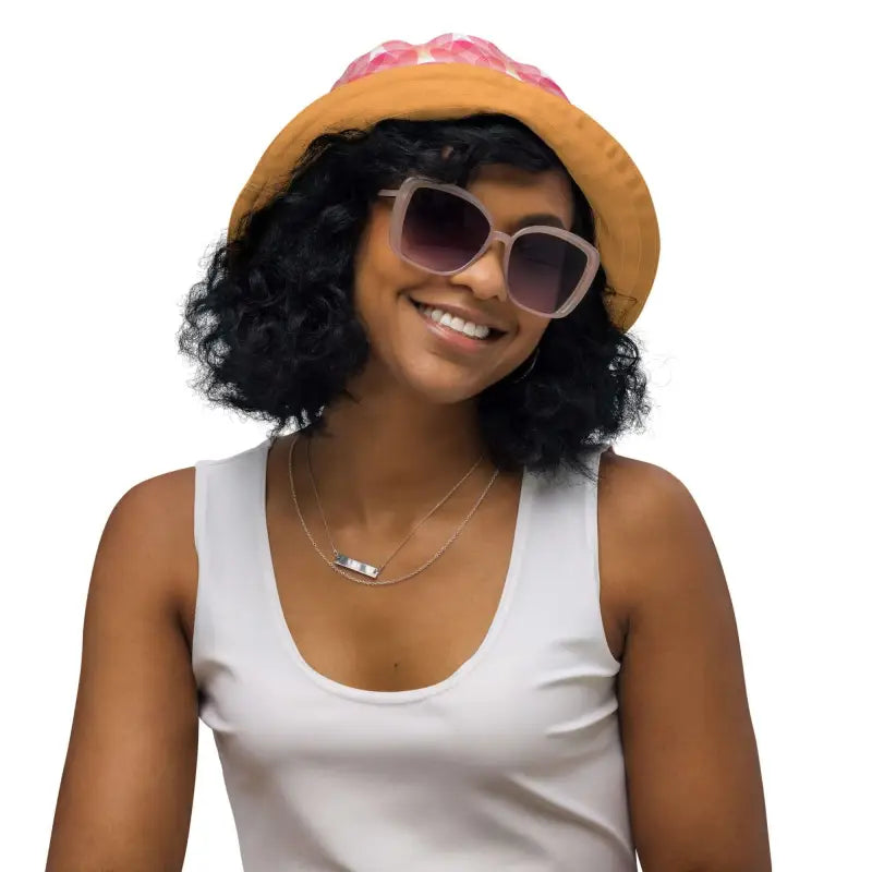 Smiling person in a yellow sun hat shows off the pink geometric print reversible bucket hat