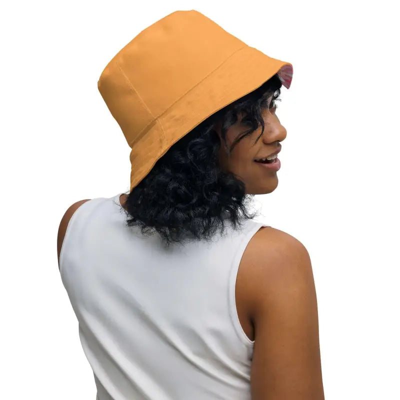 Mustard yellow bucket hat worn by a person showcasing the pink geometric print reversible bucket hat