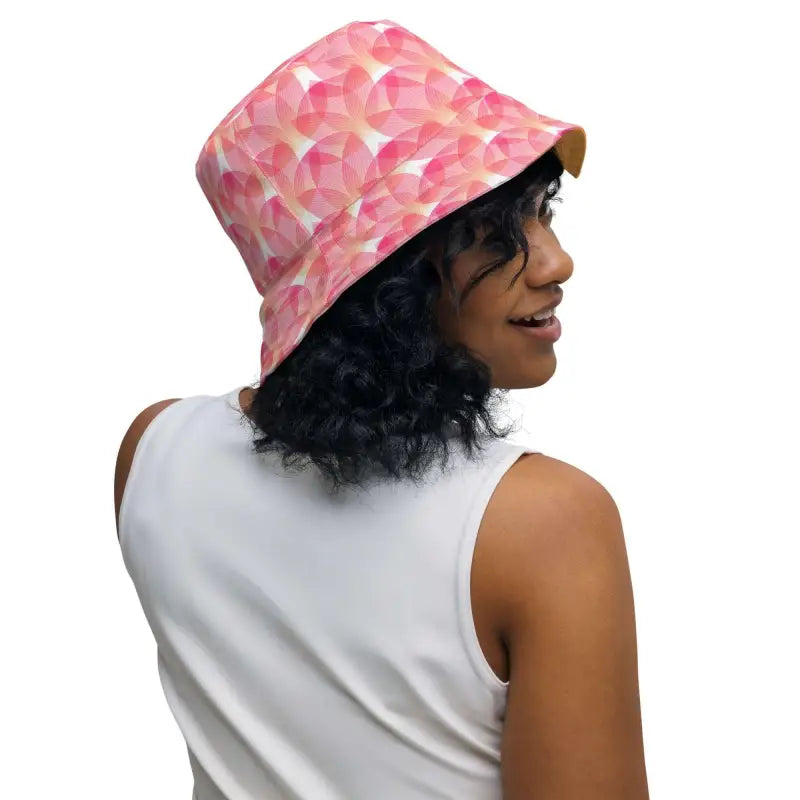 Person with curly dark hair sporting a pink geometric print reversible bucket hat
