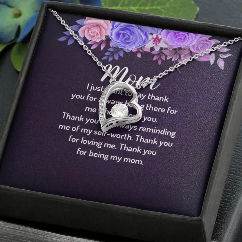 Silver love heart necklace with Mom pendant and charm on a gift box with blooms