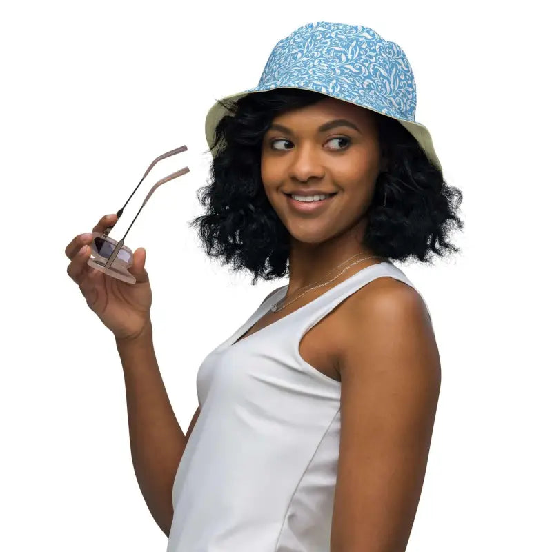 Woman in a blue floral reversible bucket hat, stylishly holding sunglasses outdoors