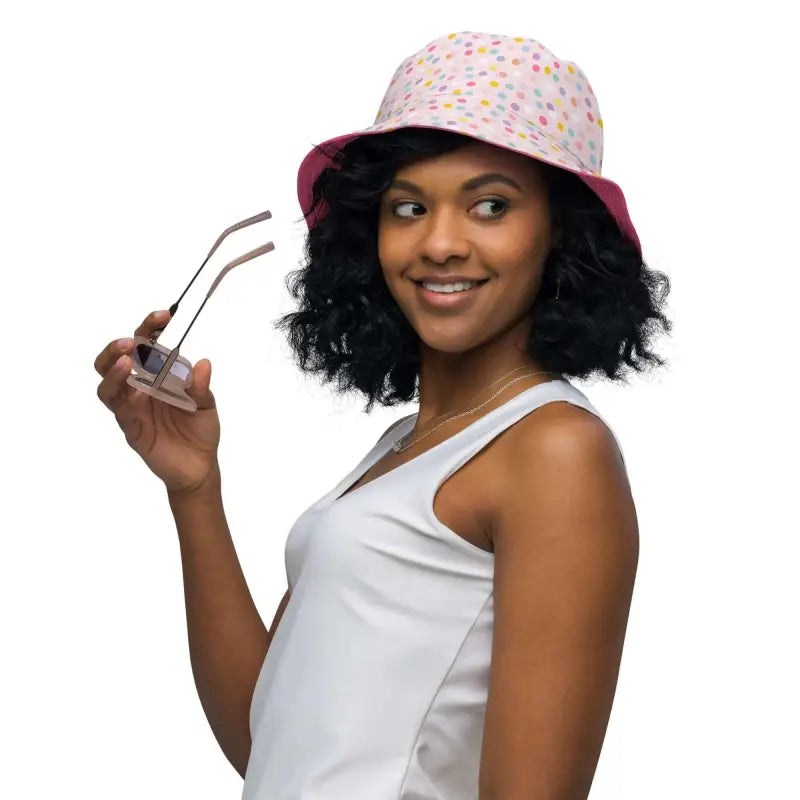 Smiling woman in a colorful polka dot reversible bucket hat holding sunglasses