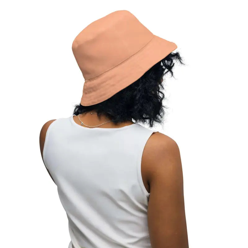 Person with dark curly hair modeling a Solid Peach Reversible Bucket Hat with a blue floral print