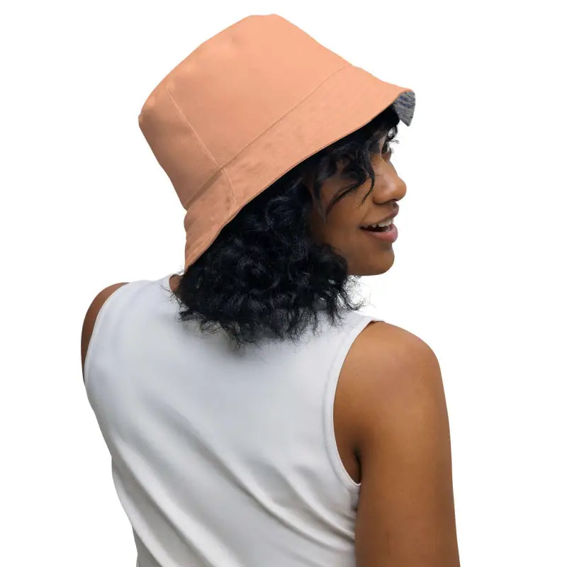 Person with curly dark hair rocks a solid peach reversible bucket hat